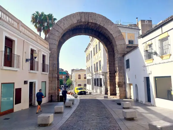 El arco en su contexto urbano, con viandantes atravesándolo, que dan la escala de sus 14 m