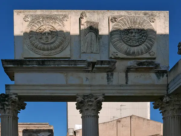 Das Gebälk mit den Schildmedaillons und den Figuren: die Reliefs des Portikus